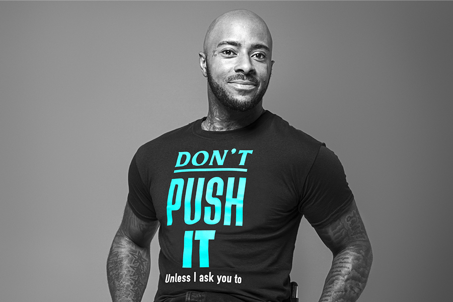 Image of a man called Ashley, sitting on a wheelchair. Ashley is wearing a t-shirt that says ‘Don’t push it, unless I ask you to.’